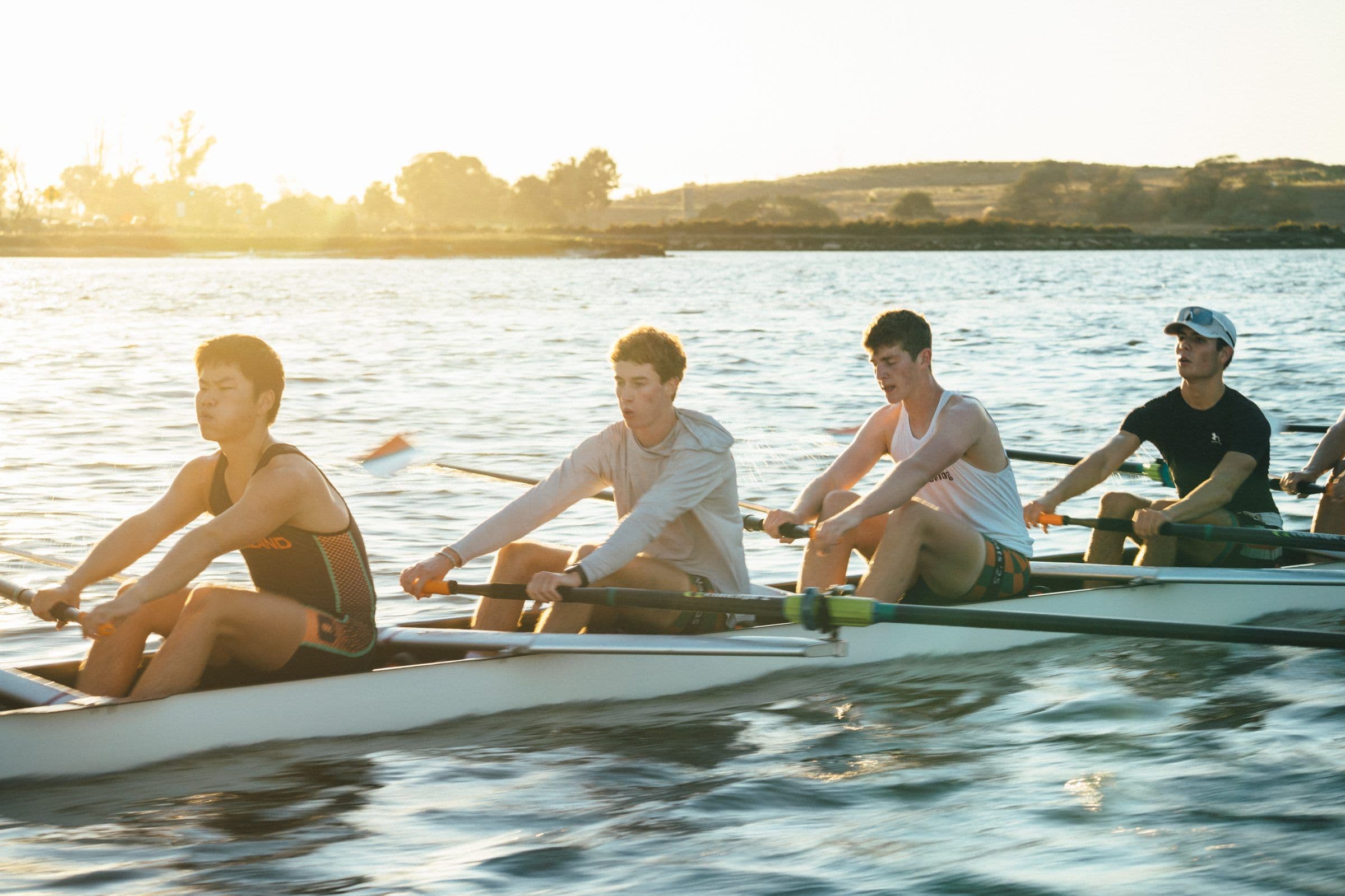 A men's crew rows into the low sun on the Estuary at the end of practice