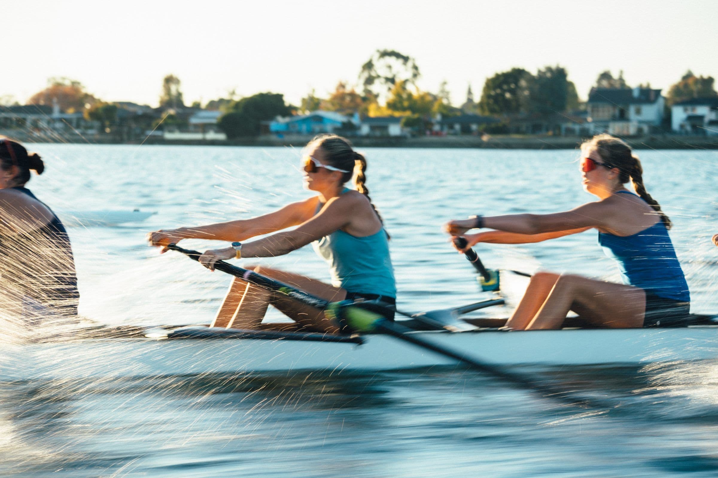 Two women's rowers drive through a piece on the Estuary in late afternoon light, spray coming off the blades