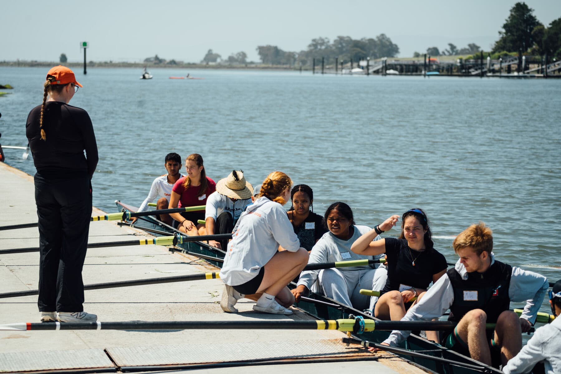 A coach steadies a boat of first-time rowers at the Tidewater dock on a bright summer day