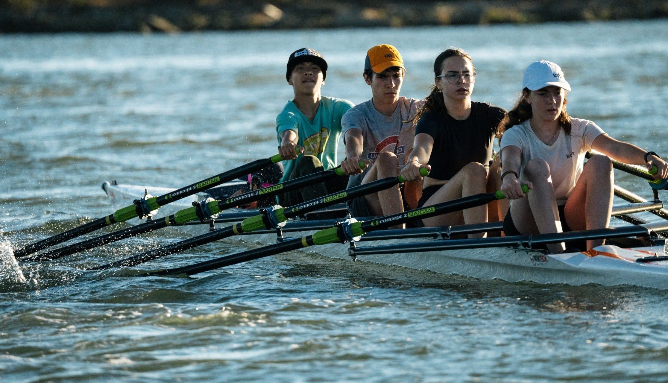 Four middle school rowers reach forward together for the next stroke on the Estuary, late afternoon sun on the water