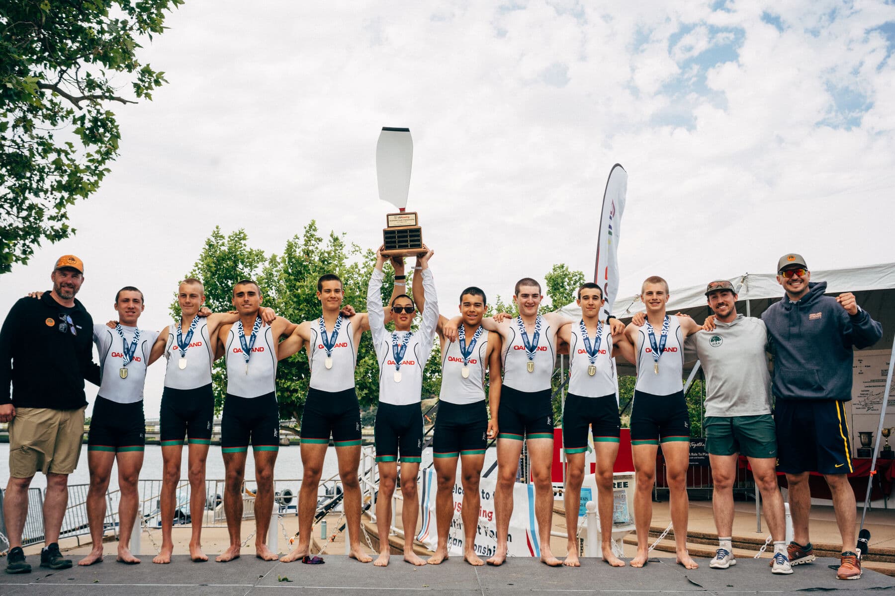 The men's U17 eight and their coaches line the dock with gold medals around their necks, the trophy held high, at the 2026 USRowing Youth National Championships