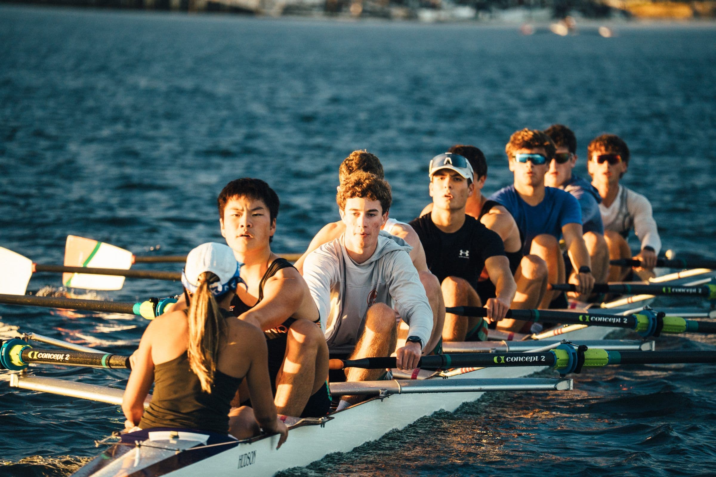 A men's eight and their coxswain look up from the water at practice