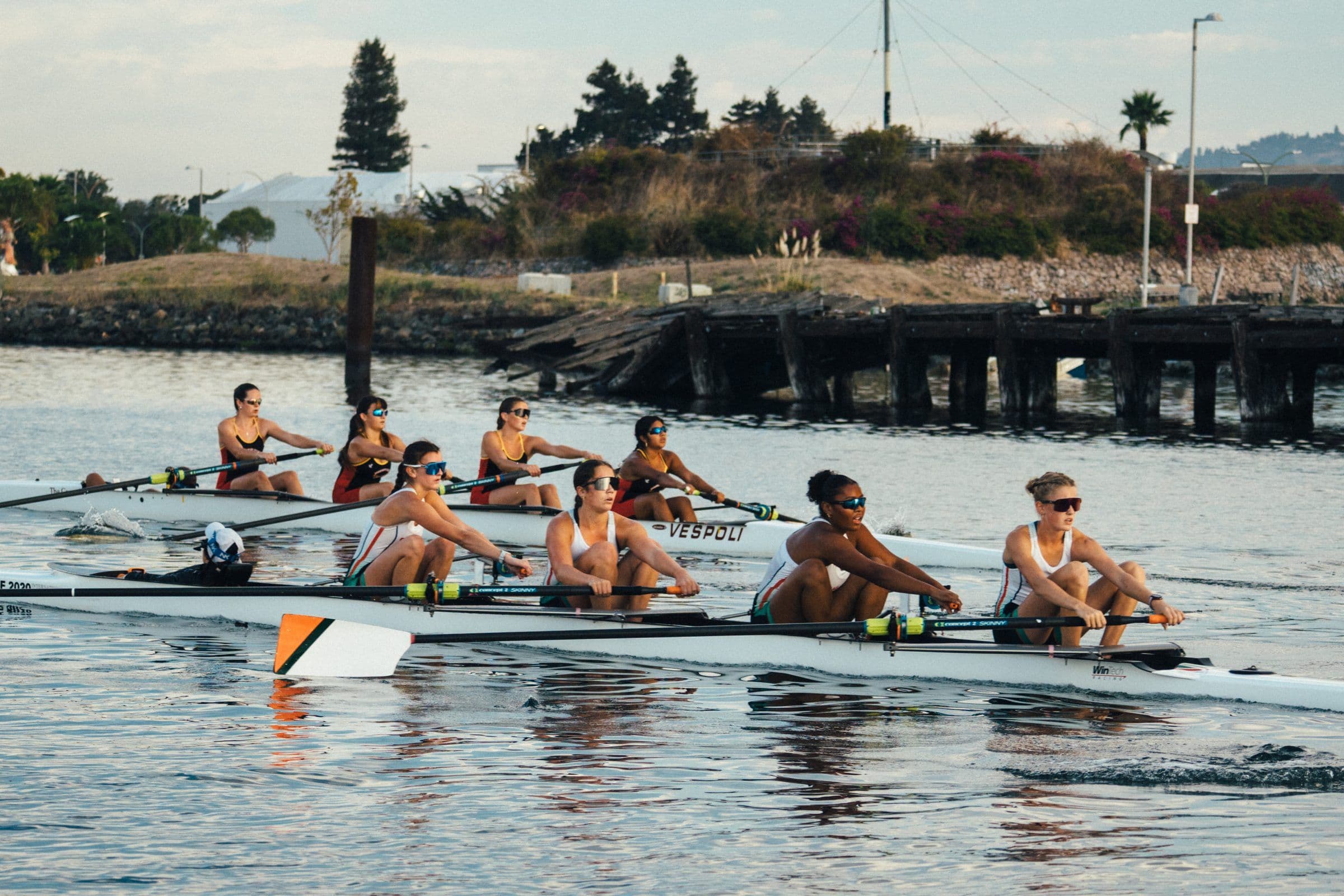 Two women's crews race side by side past an old pier at Head of the Estuary