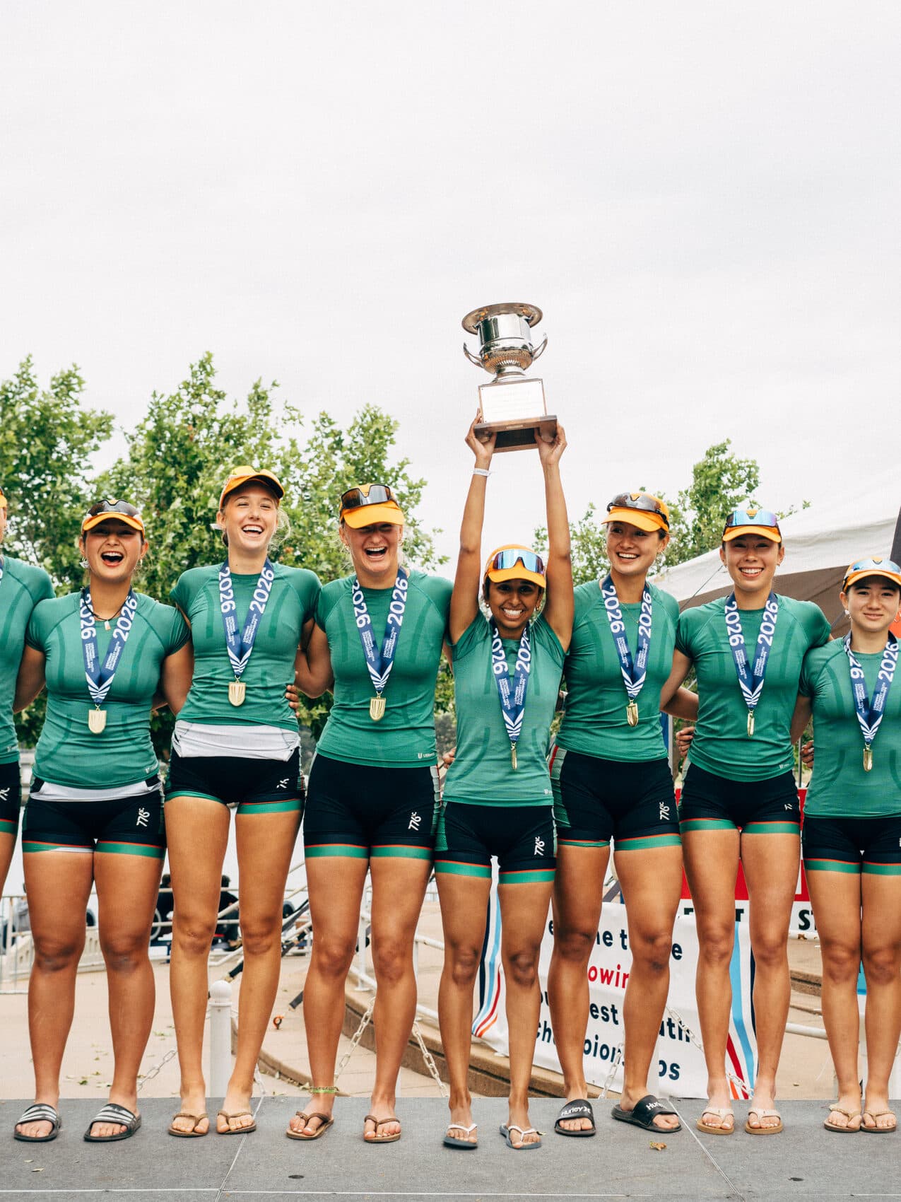 The women's crew hoists a first-place trophy together at the awards dock, medals around their necks