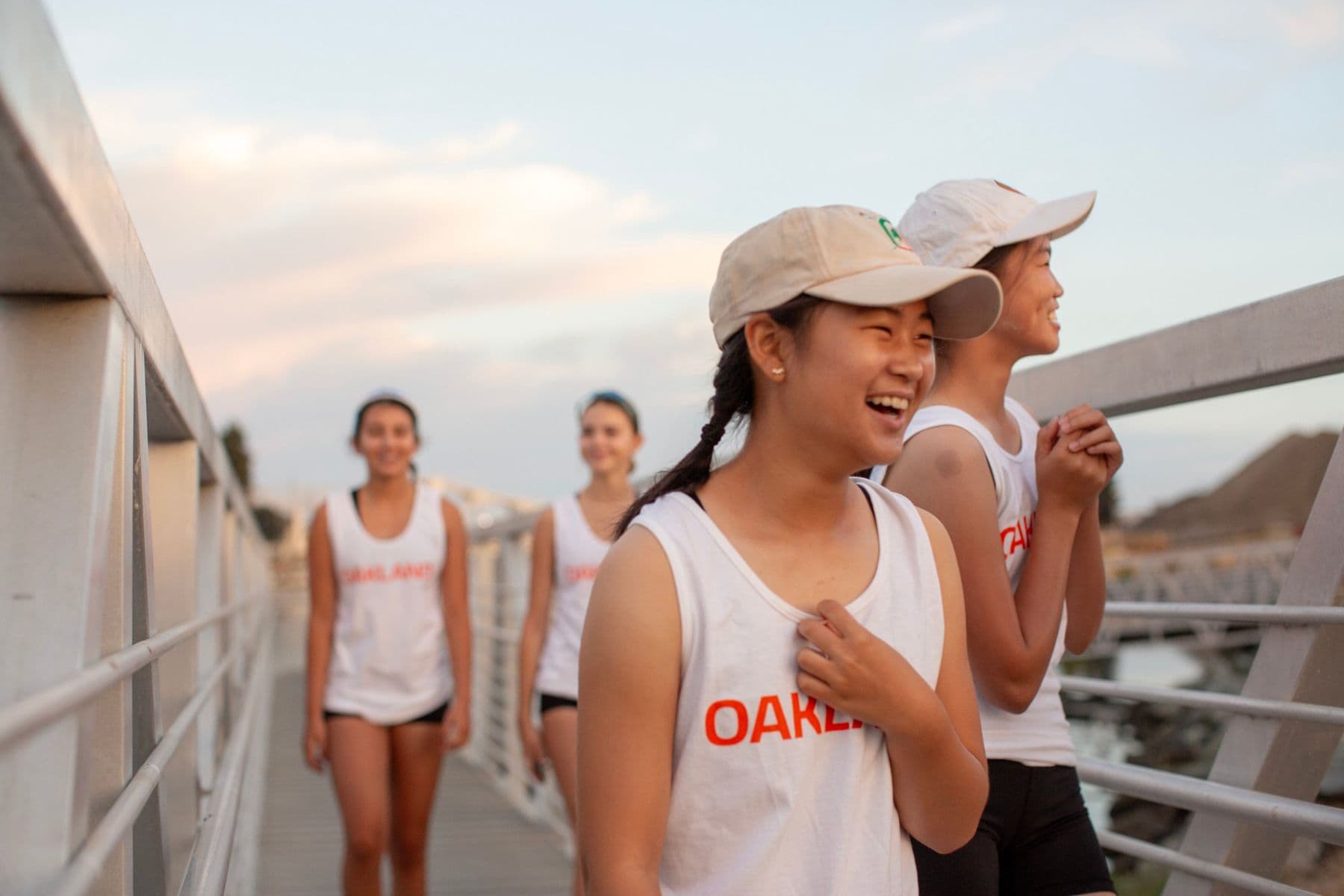 Rowers in OAKLAND tanks laugh together on the gangway on race morning
