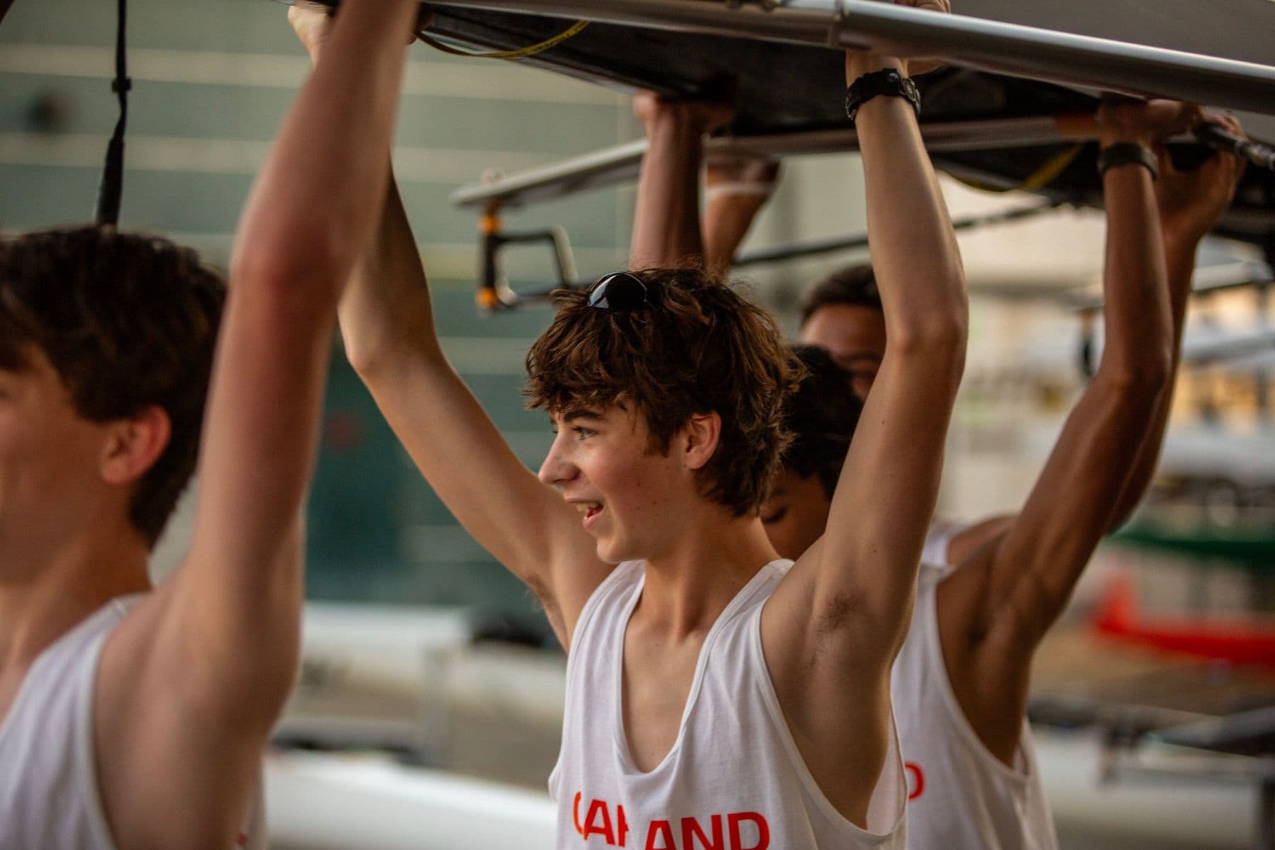 A men's rower smiles as his crew lifts their boat overhead